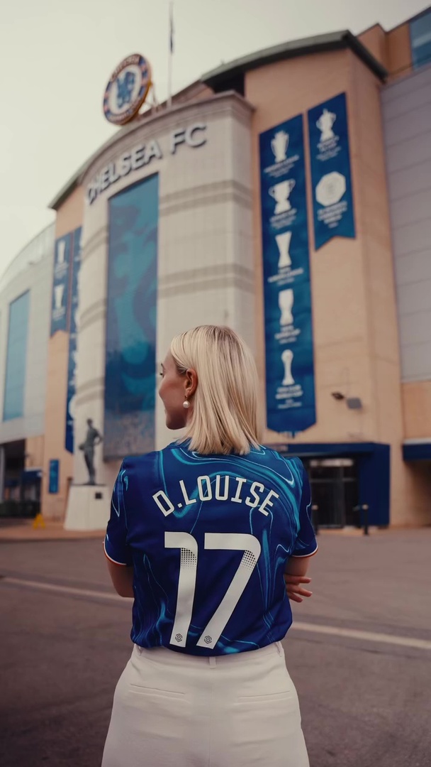 Woman in Chelsea FC jersey standing in front of the stadium.